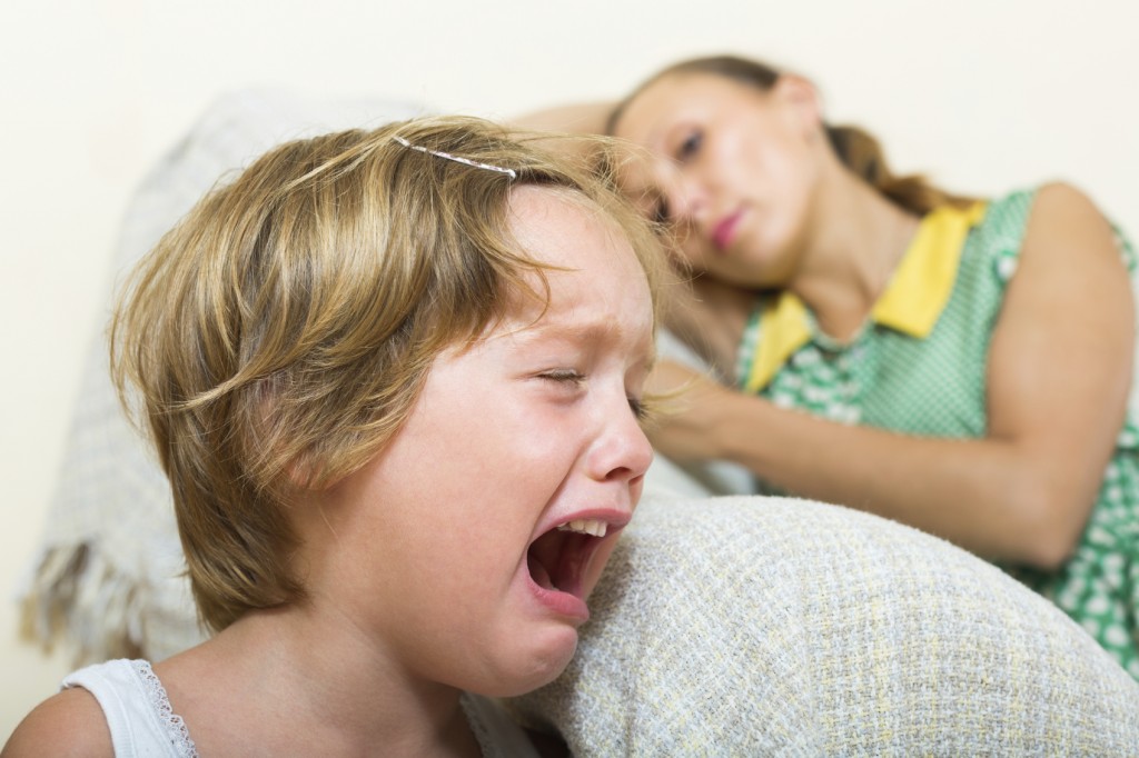 Crying little girl and upset mother sitting on couch at home