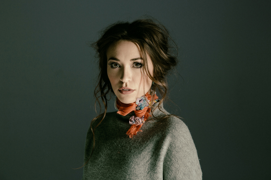 Lauren Daigle in a sweater with an orange scarf and the background is a dark blue-gray.