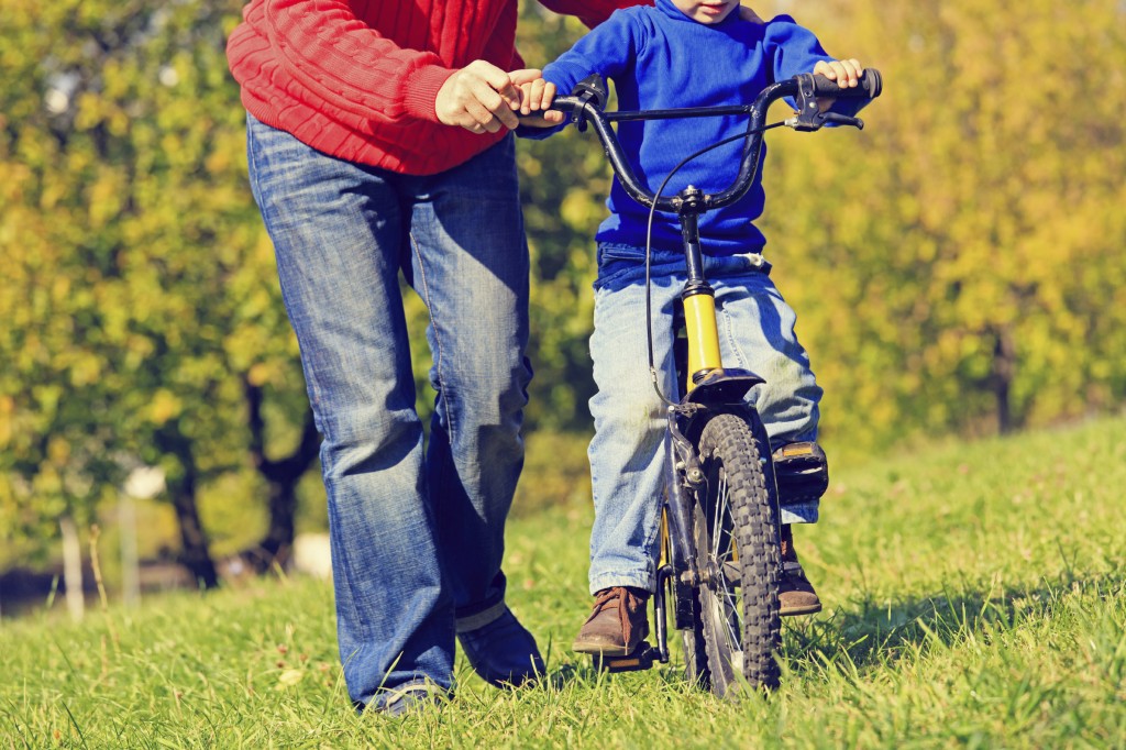 father teaches son to ride bicycle outdoors