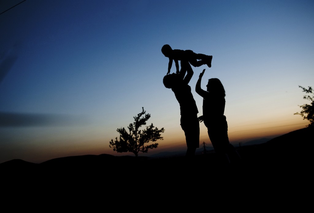 Silhouette of happy pregnant family with little boy spending time in nature