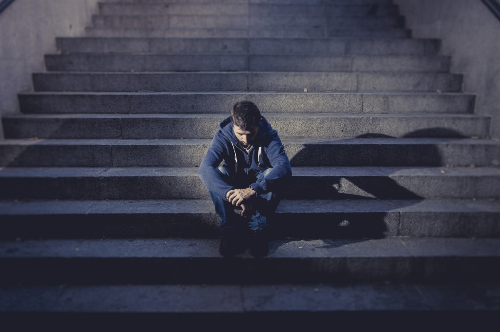 Young man lost in depression sitting on ground street concrete stairs