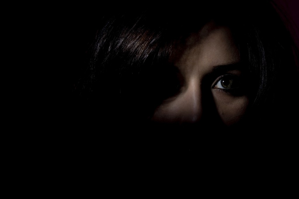 Woman stood in the dark showing half her face looking scared
