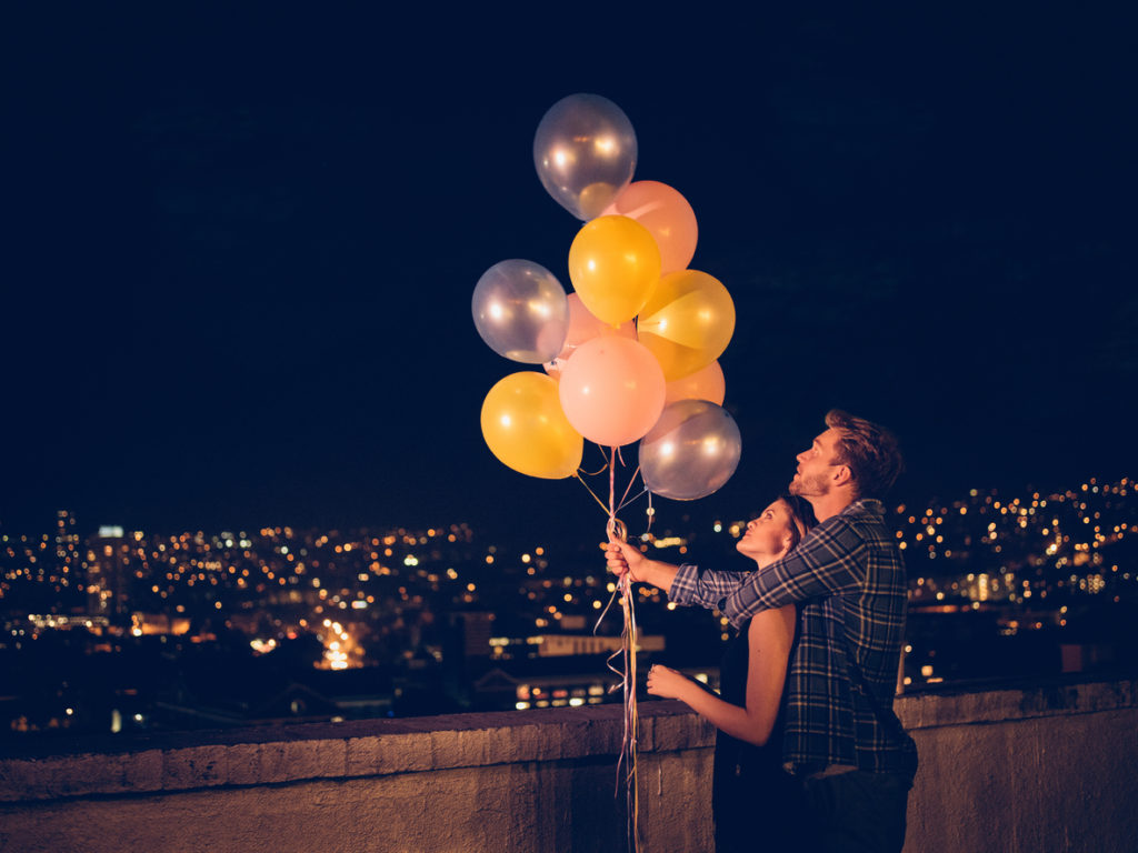 Happy young couple celebrates with colourful ballons on the rooftop